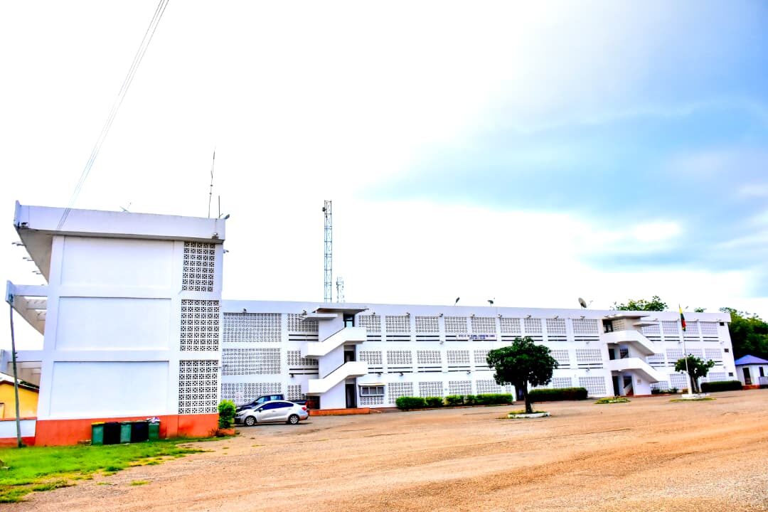 The white office building of the Council seen from the open yard, with a car parked in front and a flag on a pole.